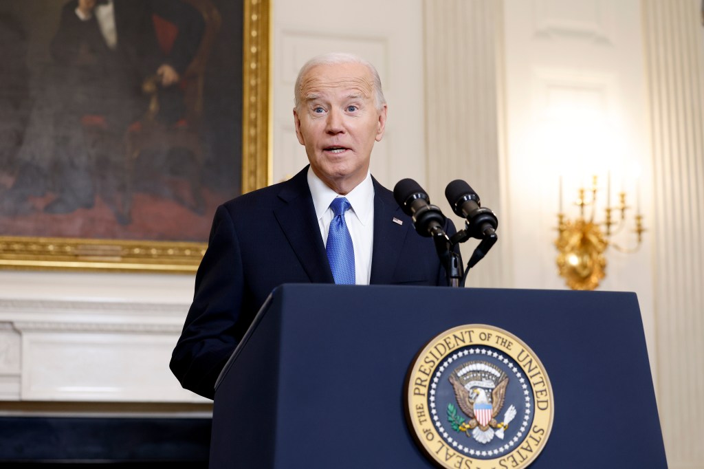 President Biden speaking at a podium with two microphones, with the Seal of the President of the United States visible.