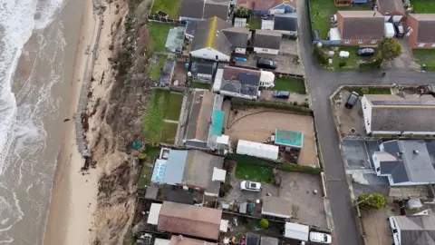 Qays Najm A drone shot above chalets and gardens along a cliff edge.