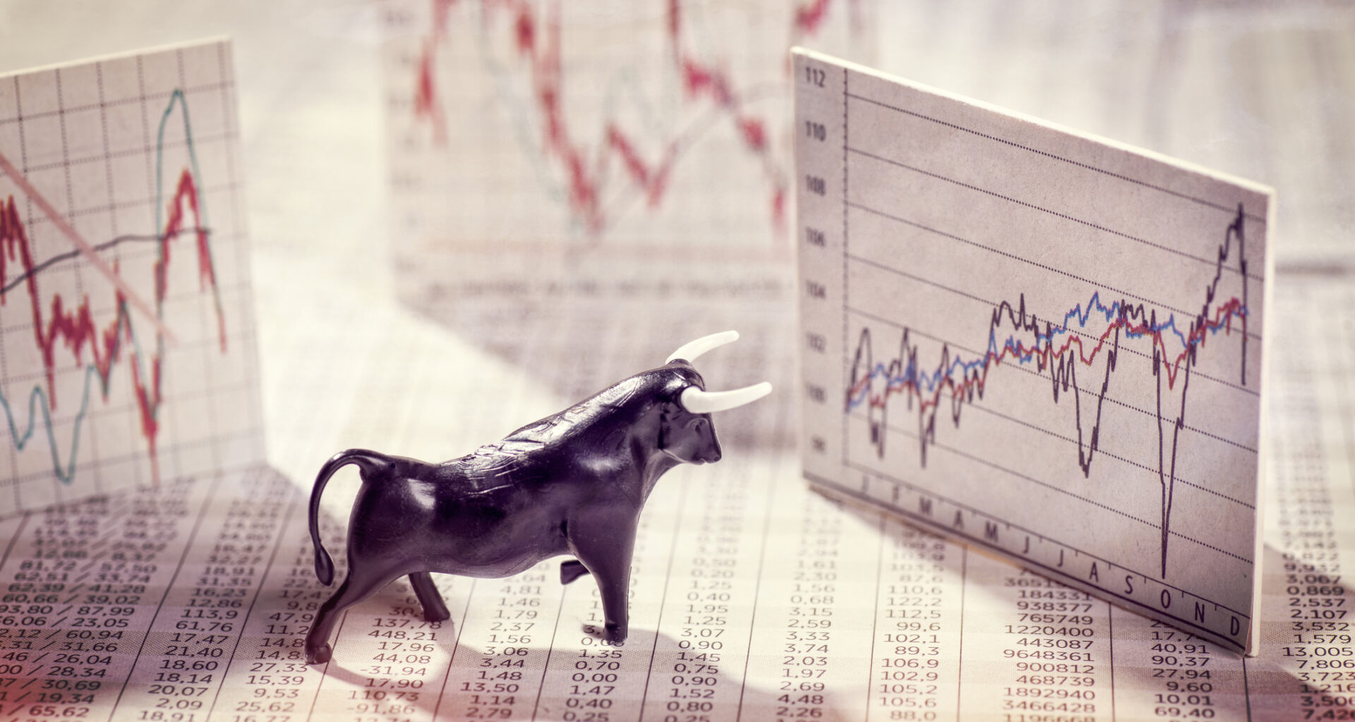 A bull figurine standing on newsprint is surrounded by index cards showing stock price chart.