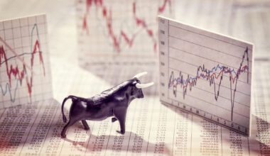 A bull figurine standing on newsprint is surrounded by index cards showing stock price chart.