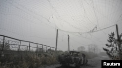 A burned pickup vehicle under a torn anti-drone net in the middle of a road near Hulyaypole.
