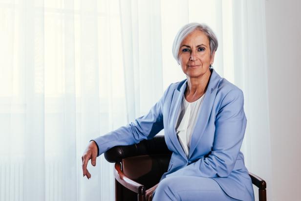 Anna Sporrer sitzt auf einem Stuhl vor einem Fenster.