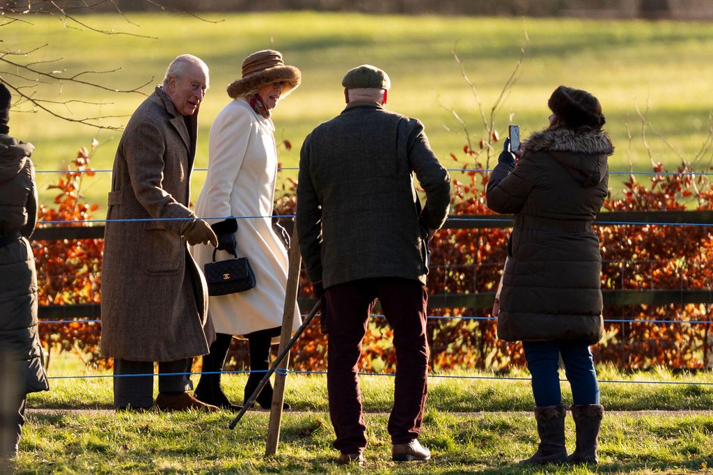 King Charles III and Queen Camilla walking to church with lady taking photo of them