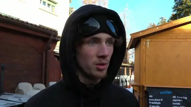 Axel Clavier speaks is seen wearing a black hoodie and a hat with googles on the front