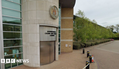 Google Street View of the front of Bournemouth Crown Court. The revolving doors are closed and a sign in black writing above the door says Bournemouth Crown and County Courts. Above the sign on the round entranceway is a round crest with a central badge flanked by a lion and a horse.