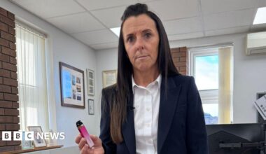 Head teacher wearing navy suit holds up a pink vape