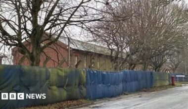 Exterior shot of large brick building with barbed wire surrounding it on a road
