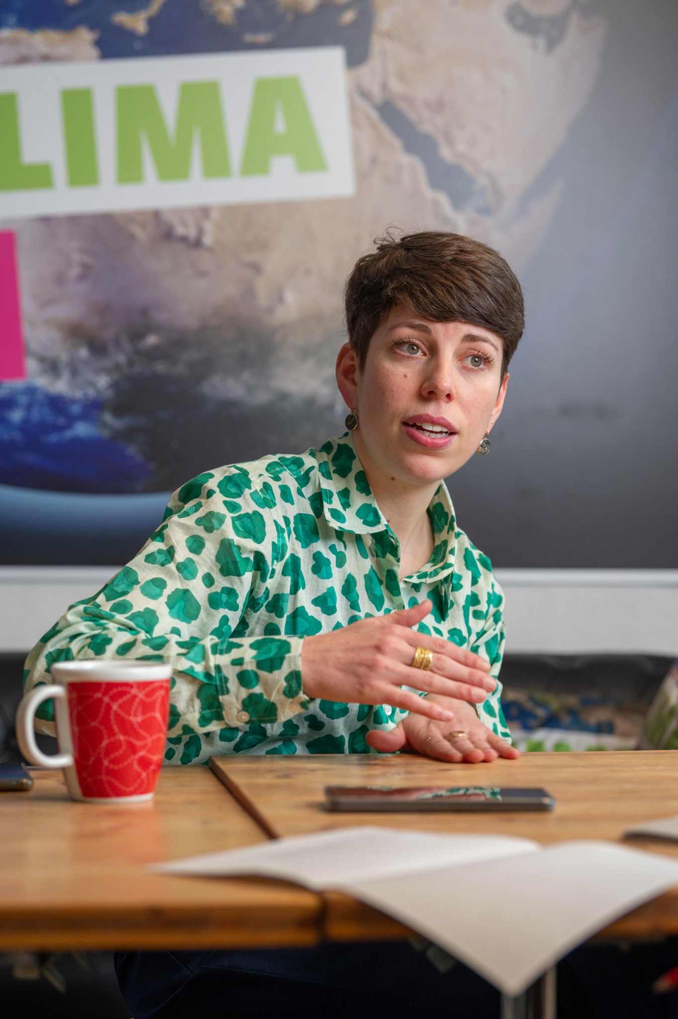 Lisa Mazzone, membre des Verts suisses, discutant à une table, avec une affiche sur le climat en arrière-plan.