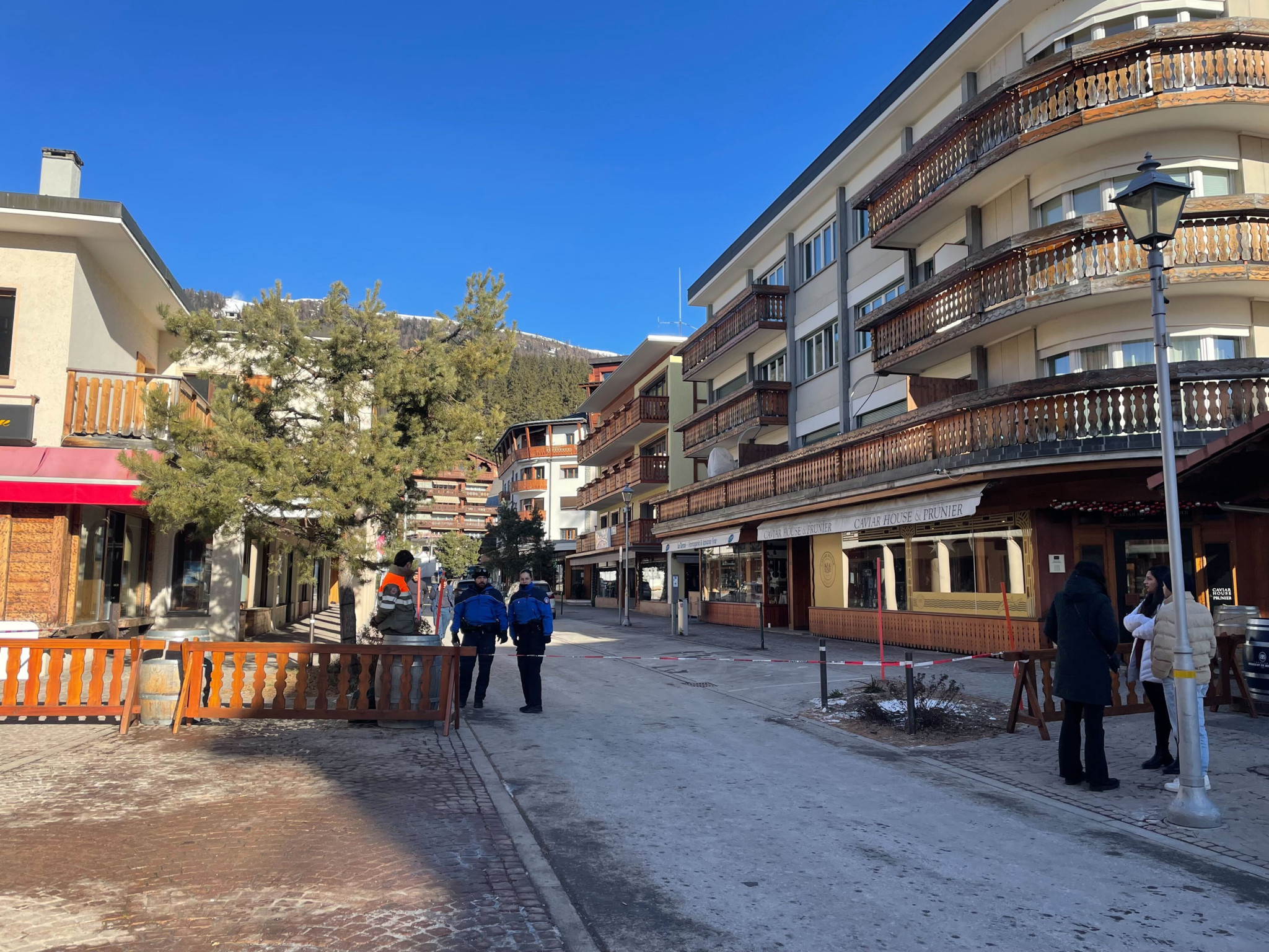 Fussgängerzone mit Menschen und Wohnhäusern in einer Bergstadt bei sonnigem Wetter.