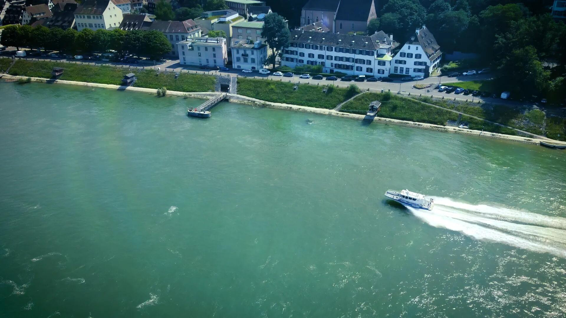 Drohnenansicht eines Flusses mit einem Schnellboot auf dem Wasser, das an einem Ufer mit Häusern und Bäumen vorbeifährt.