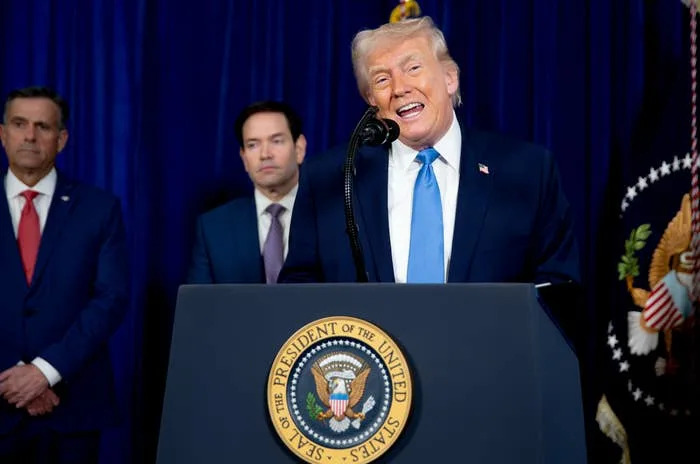 Donald Trump speaks at a podium with the U.S. presidential seal, flanked by two other individuals in suits, in a formal setting