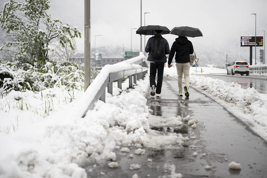 Zwei Personen gehen auf einem teilweise vom Schnee geraeumten Buergersteig auf einer Bruecke ueber die Autobahn zwischen zwischen Interlaken-West und Interlaken-Ost am Donnerstag, den 17. April 2025 i ...