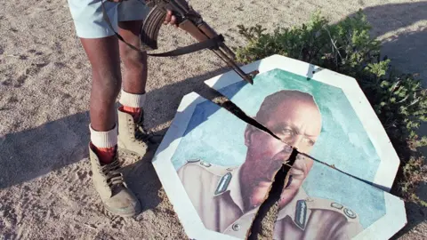 AFP/Getty Images A militia man (face not visible) in boots standing over a broken portrait of Siad Barre with his gun.