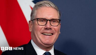 Keir Starmer smiling widely in front of a Union Jack on the wall behind him
