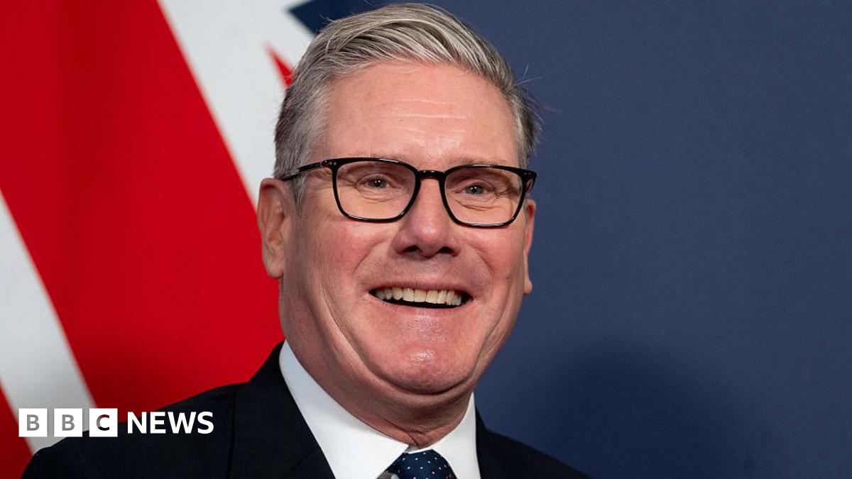 Keir Starmer smiling widely in front of a Union Jack on the wall behind him