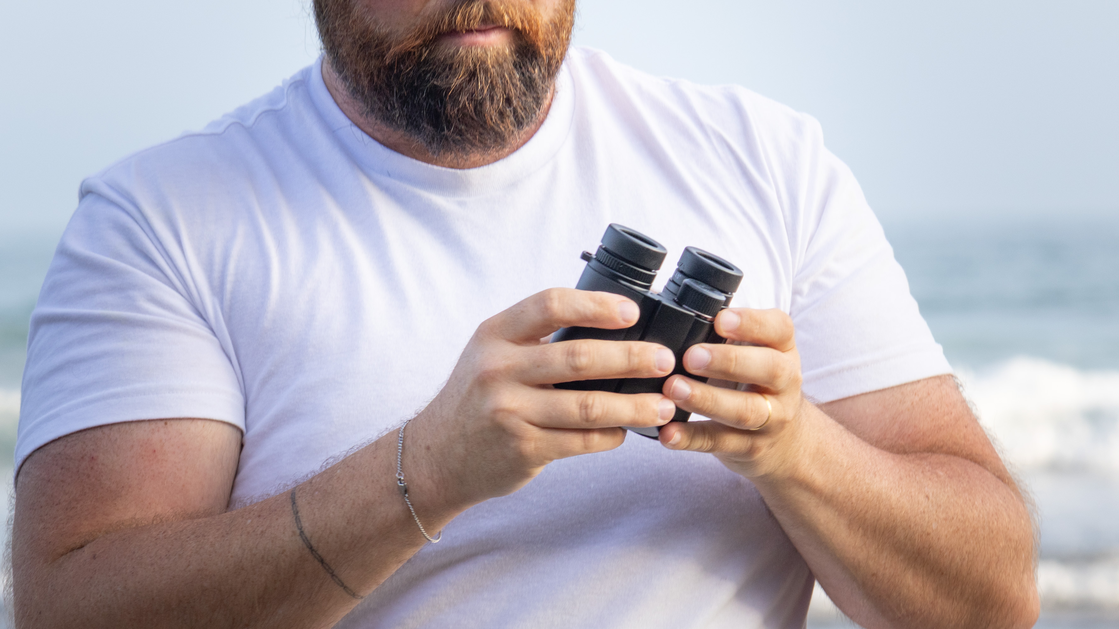 Nikon Stabilized 12x25 S binoculars held in the hands of the reviewer in front of breaking waves at the beach