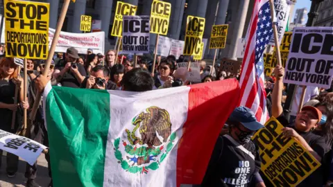 EPA A person holds a Mexican flag behind them in a crowd of protesters in Manhattan on 10 June 2025