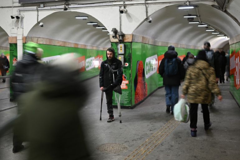 TOPSHOT - Pedestrians walk past an amputee begging for alms at a metro station during an air raid alert in Kyiv on January 26, 2026, amid the Russian invasion of Ukraine. (Photo by Sergei GAPON / AFP)