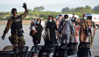 U.S. Navy personnel greet Afghan evacuees arriving at an airfield, wearing masks amid security processing during the refugee relocation operation. (Photo Credit: EPA)