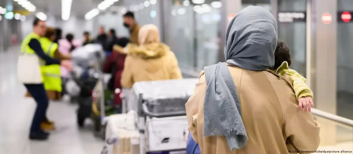 Afghan refugees with luggage wait at an airport terminal as Germany transfers individuals from Pakistan to Berlin under the admission program. (Photo Credit: Jule Hegerscultez/dpa/picture alliance)