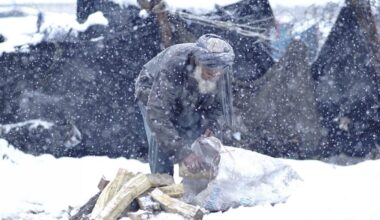 An elderly Afghan man struggles through heavy snowfall while trying to start a fire for warmth, highlighting the harsh winter conditions faced by millions in need of humanitarian assistance across Afghanistan. (Photo Credit: OCHA Afghanistan)