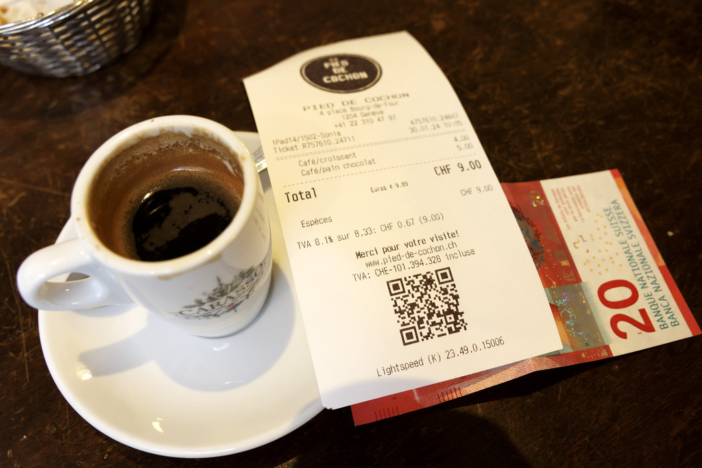 Un ticket de caisse montrant une TVA de 8,1% à côté d’une tasse de café et d’un billet de 20 francs suisses, à Genève.
