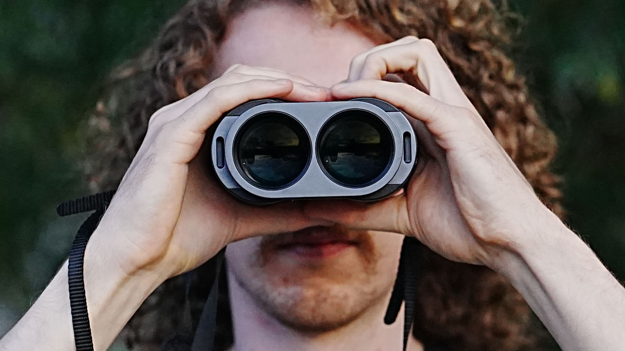 A close-up of a man holding and looking through the Fujifilm Techno-Stabi TS-L 1640 image-stabilized binoculars