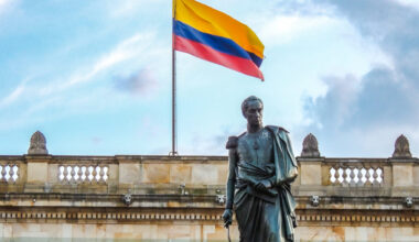 the statue of Simón Bolívar standing before Colombia’s National Capitol, with the flag waving