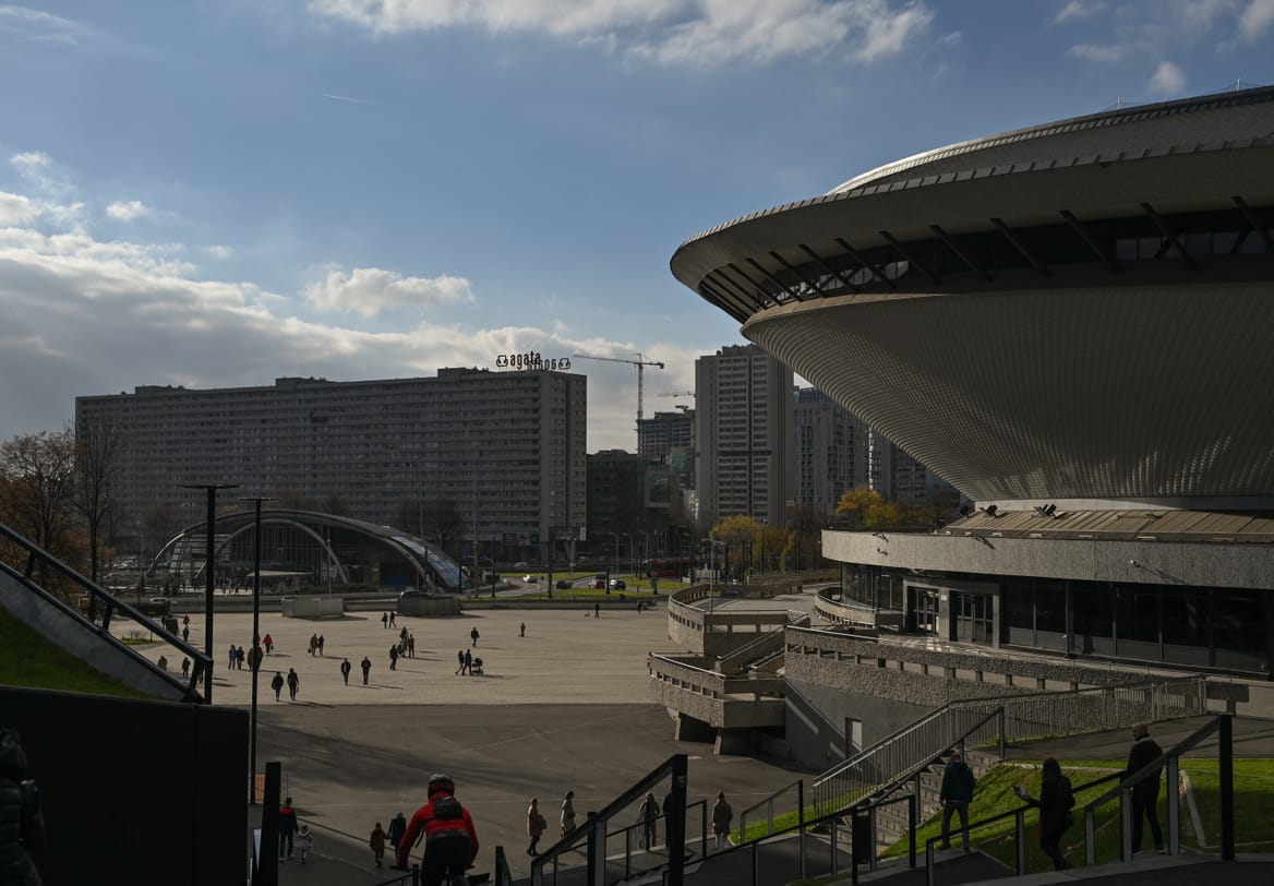 The edge of the orb-like Spodek arena overlooking a city plaza with people and other buildings in the distance