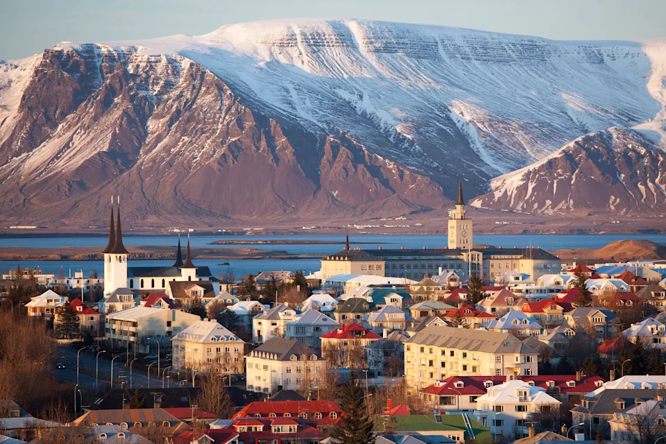 The city of Reykjavik, Iceland, in wintry sunlight with snowy mountains in the background.
