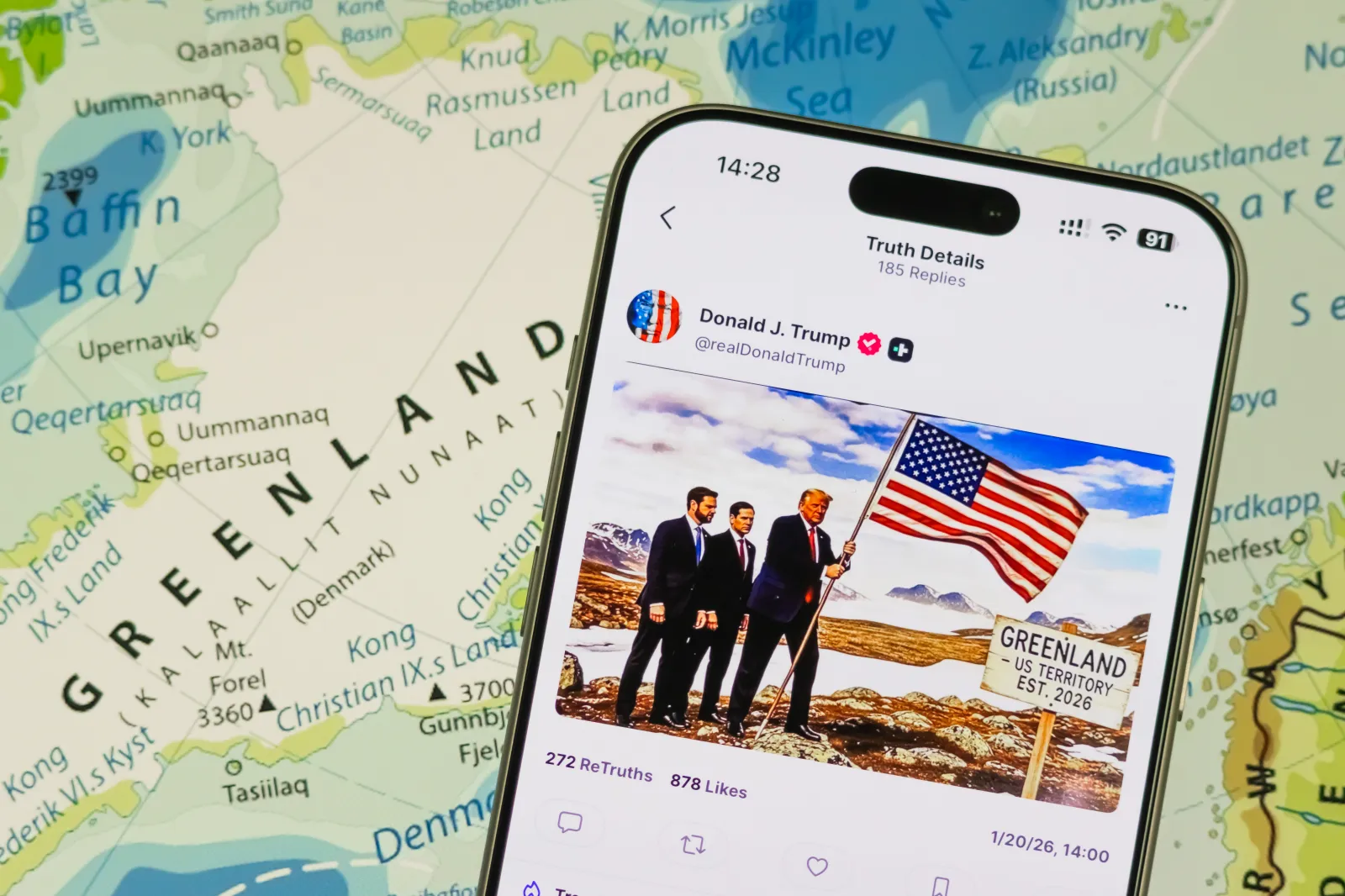 A smartphone displays a post by U.S. President Donald Trump on the Truth Social platform showing a composite image featuring Trump alongside U.S. Secretary of State Marco Rubio and U.S. Vice President J.D. Vance, with the U.S. flag and a sign reading Greenland, U.S. Territory Est. 2026, while a map of Greenland is visible in the background, on January 20, 2026.