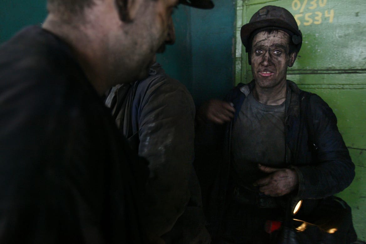 Three miners, one of whom is looking at the camera, his face covered with coal dust