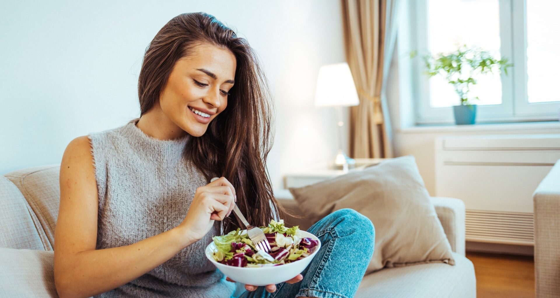 Close up portrait of young woman while she eats tasty vegan salad at home.