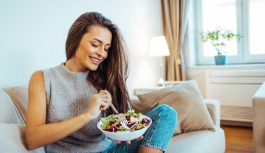 Close up portrait of young woman while she eats tasty vegan salad at home.