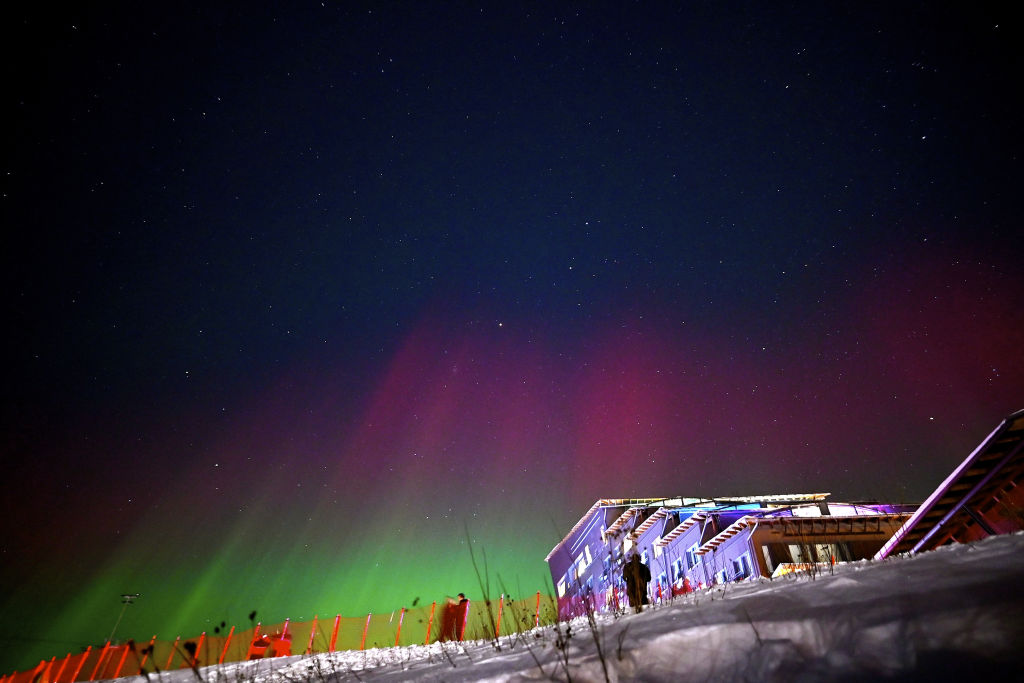 northern lights above a ski slope fill the sky with red and green auroras.