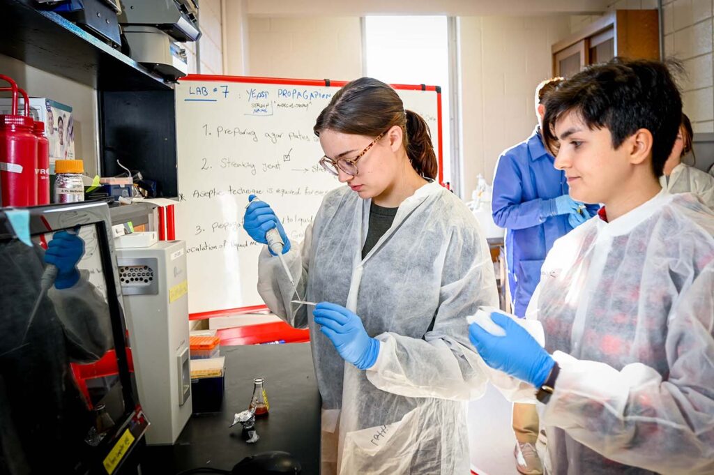 two young women wearing disposable lab coats and blue latex gloves conduct experiments in a food science lab at NC State