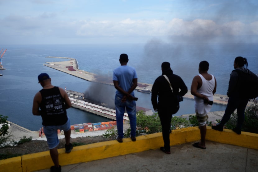 Men watch smoke rising from a dock after explosions were heard at La Guaira port, Venezuela,...