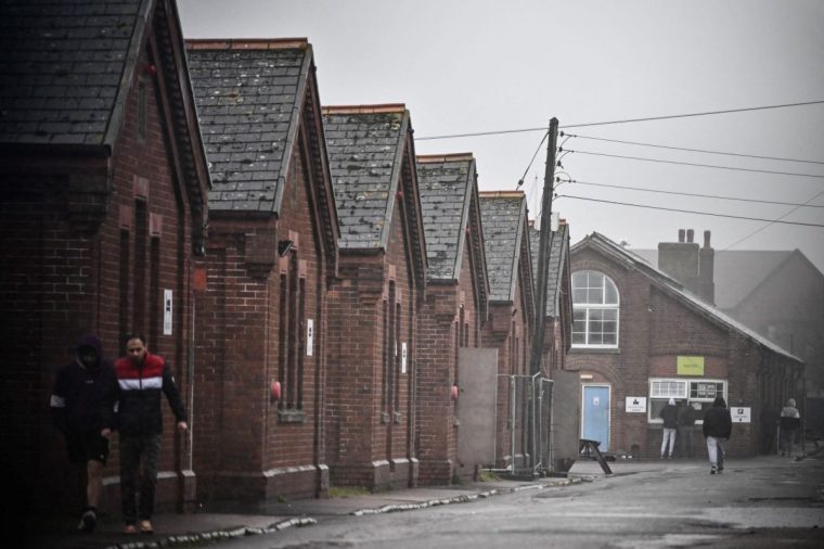 Residents of Napier Barracks, a former military barracks that is being used to house asylum seekers, walk under the rain among the buildings, in Folkestone, southeast England on March 9, 2023. - The Conservative government intends to outlaw asylum claims by all illegal arrivals and transfer them elsewhere, such as Rwanda, in a bid to stop thousands of migrants from crossing the Channel on small boats. But rights groups and the United Nations said the legislation would make Britain itself an international outlaw under European and UN conventions on asylum. (Photo by Ben Stansall / AFP) (Photo by BEN STANSALL/AFP via Getty Images)