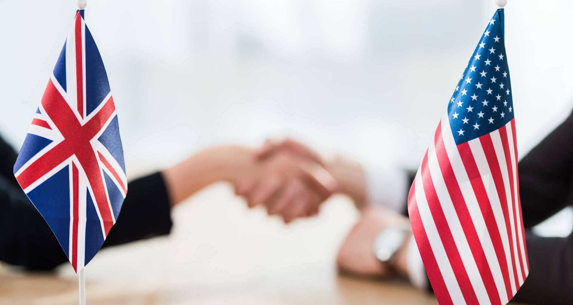 US and UK flags with a selective focus on diplomats shaking hands. Licensed by Envato Elements