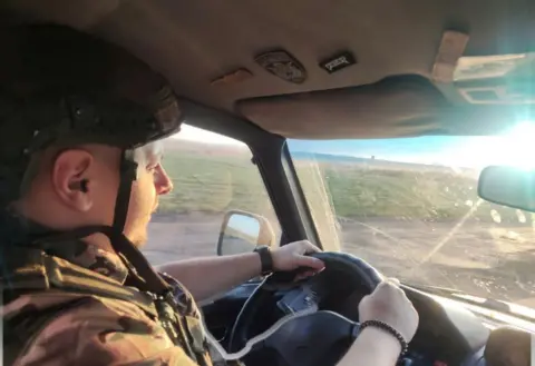 Supplied A man, in military uniform, drives a car