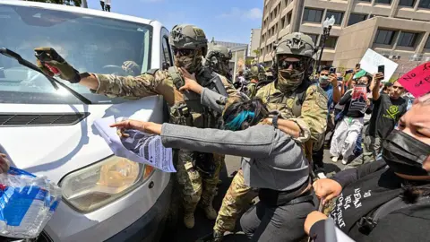 Getty Images Two police officers drag a woman away from a white van, while one aims pepper spray