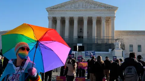 Getty Images A protester with a rainbow coloured umbrella stands outside the US Supreme Court