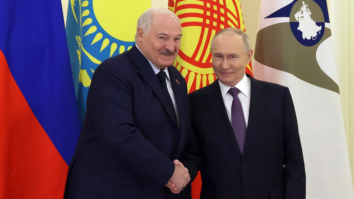 Putin and Lukashenko in dark suits greet each other with a handshake at a formal international meeting.
