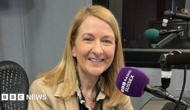 Katy Bourne sitting in a recording booth in front of a purple microphone which has "BBC RADIO SUSSEX" on it.