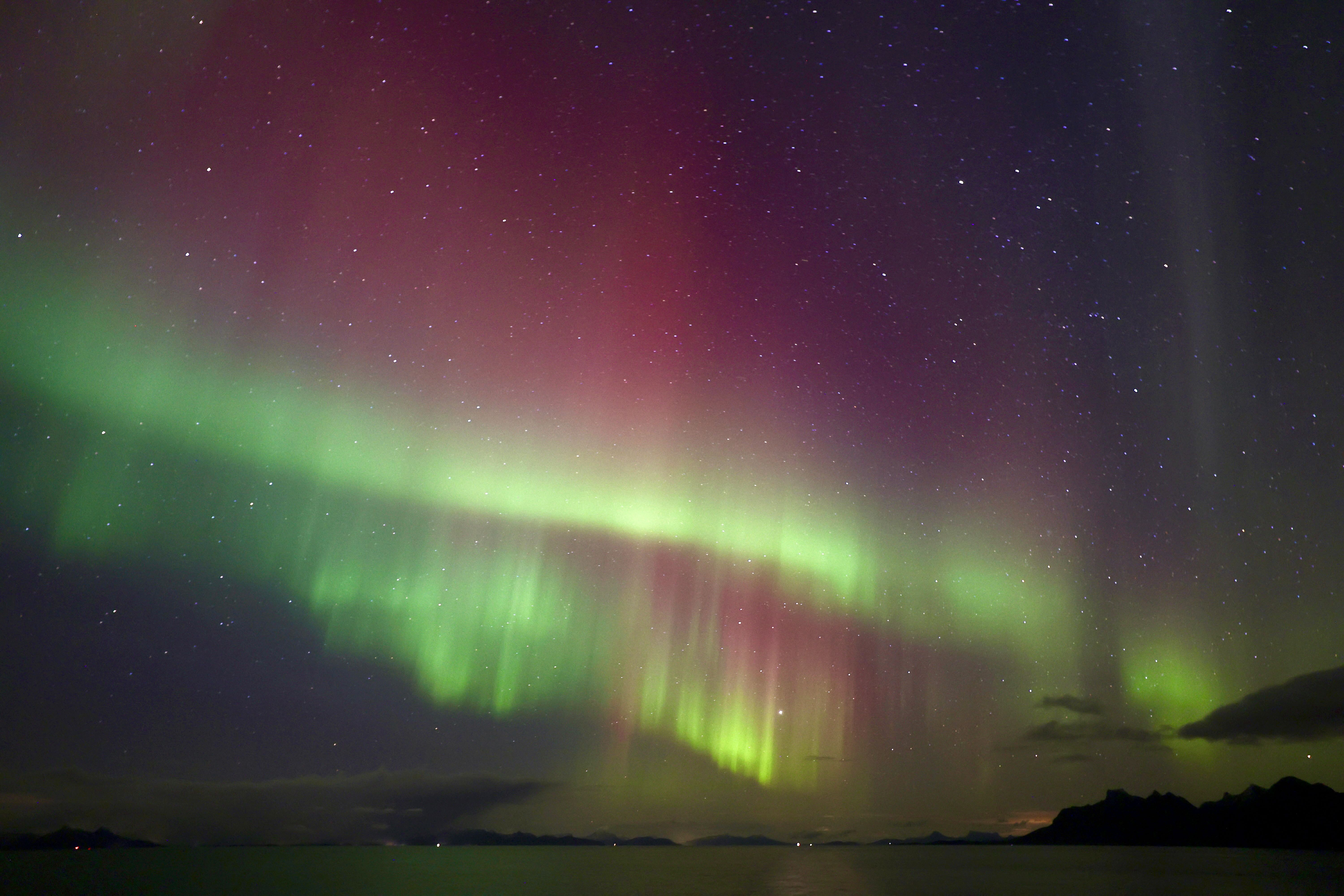 northern lights appear as huge curtains in the sky colored green and pink.
