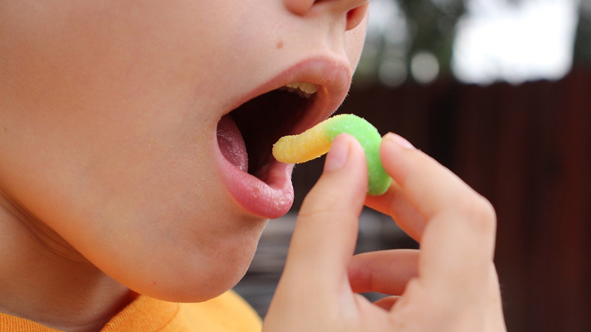 Close-up of young put putting a gummy worm candy in his mouth.
