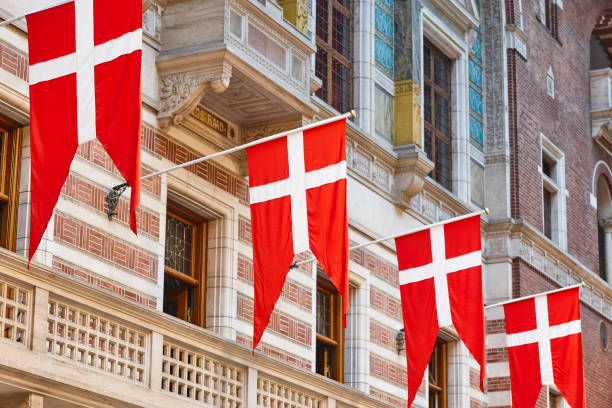 Red and white Danish flags hang from the facade of a historic building with decorative architectural details.