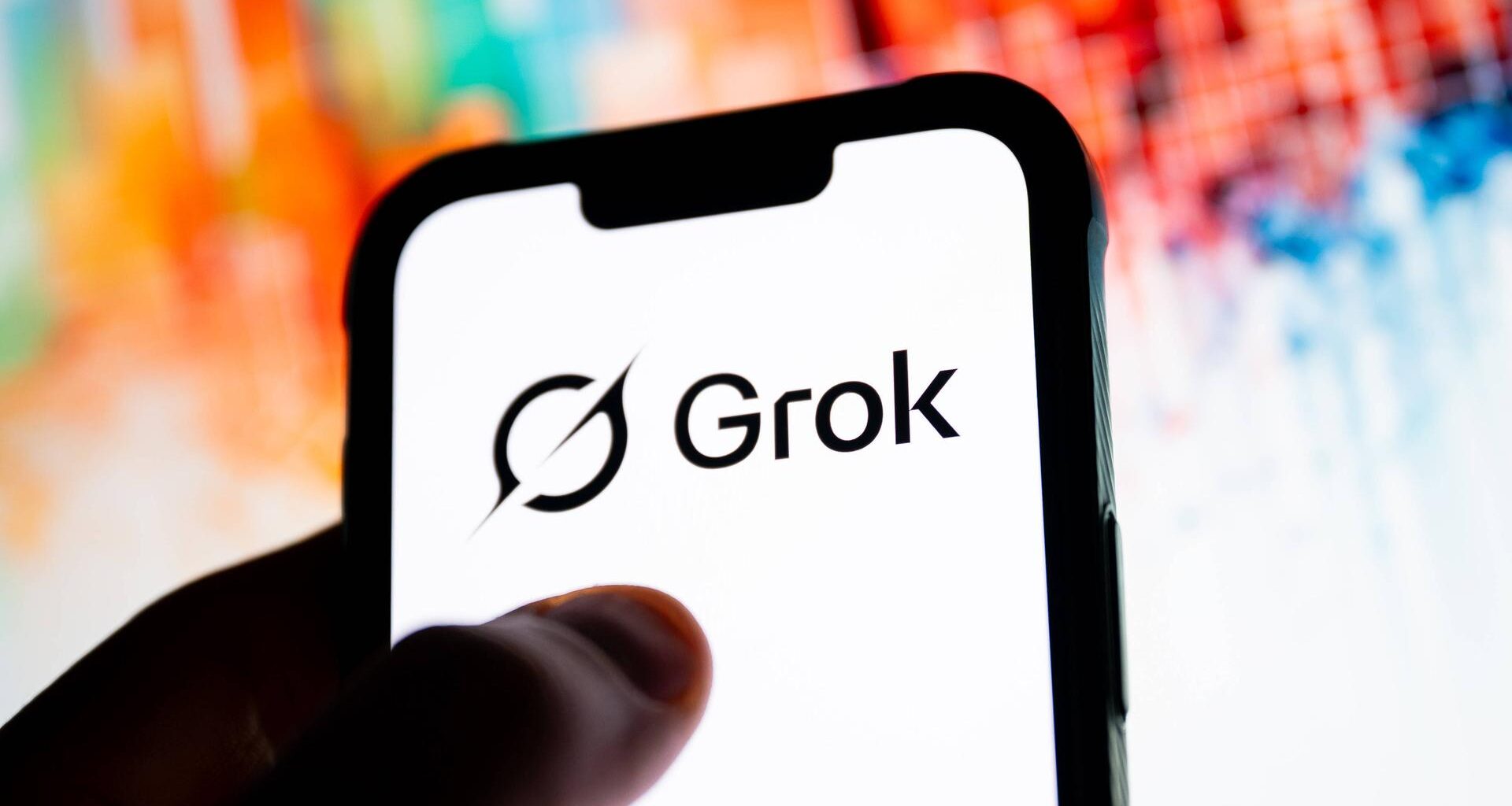 Ein alös Silhouette Daumen auf einem weißen Smartphone-Screen, auf dem in schwarz "Grok" steht. Dahinter ein bunteer Hintergrund.