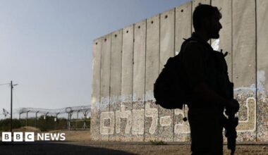 An Israeli soldier on patrol beside a protective security barrier decorated with graffiti that reads "Path for Peace" in Hebrew near the border fence with Gaza Strip, left, in the moshav Netiv HaAsara.