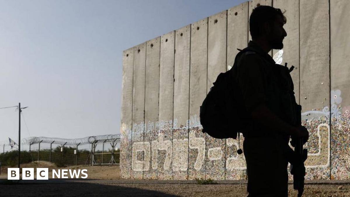 An Israeli soldier on patrol beside a protective security barrier decorated with graffiti that reads "Path for Peace" in Hebrew near the border fence with Gaza Strip, left, in the moshav Netiv HaAsara.